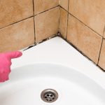 A person in a pink glove is caulk cleaning a bathtub.